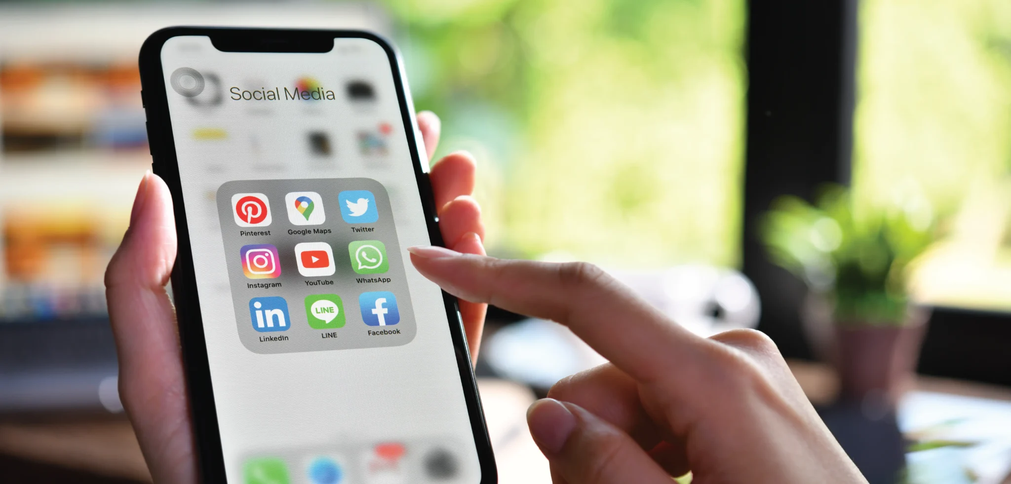 A hand holds an iPhone with a folder titled "Social Media" containing social media apps